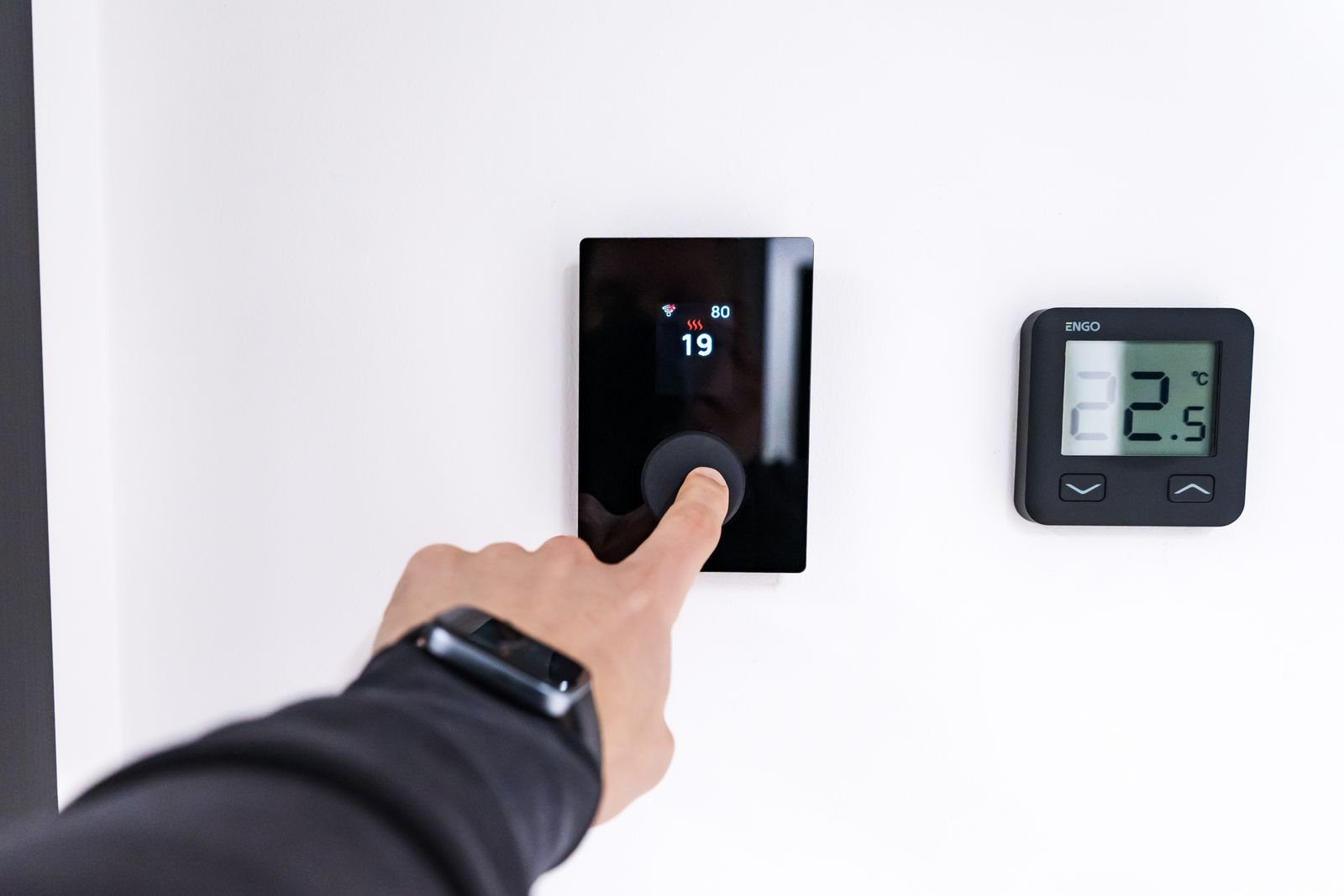 A hand adjusting a digital home thermostat on the wall